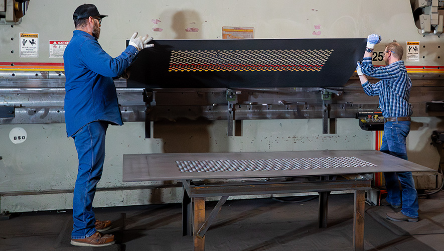 Two men working on a steel truck part