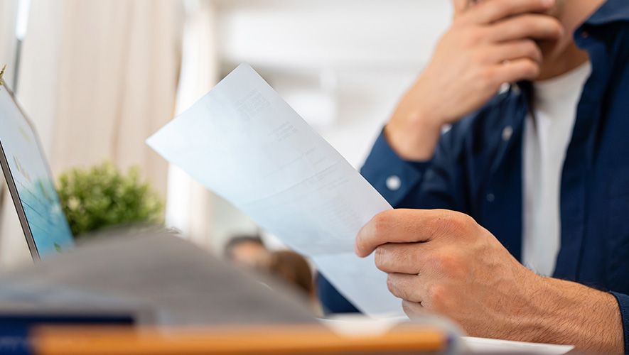 A man looking at a sheet of paper in front of a computer
